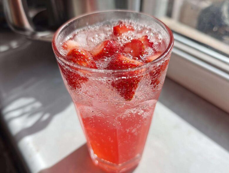 Close-up of a tall glass filled with bubbly Iced Strawberry Hibiscus Tea Lemonade and fresh strawberry slices.