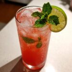 Close-up of a tall glass filled with Iced Watermelon Lime Cooler, ice, mint, and a lime wheel garnish.