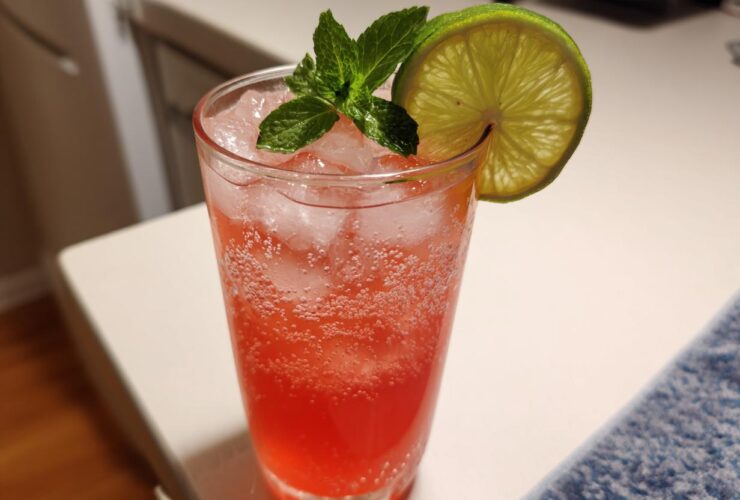 A tall glass filled with a bubbly, pink Iced Watermelon Lime Cooler, garnished with mint and a lime wheel.