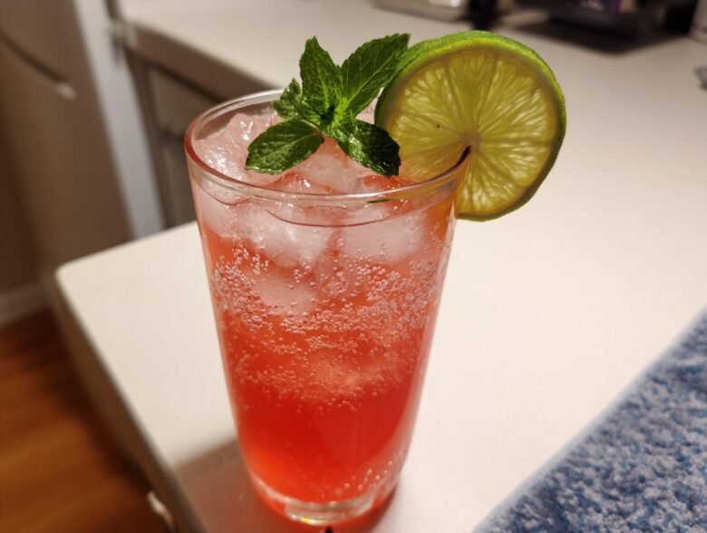 A tall glass filled with a bubbly, pink Iced Watermelon Lime Cooler, garnished with mint and a lime wheel.