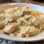 Close-up of a serving of Instant Pot Creamy Chicken and Orzo in a white bowl, featuring tender chicken pieces mixed with orzo pasta in a rich sauce.