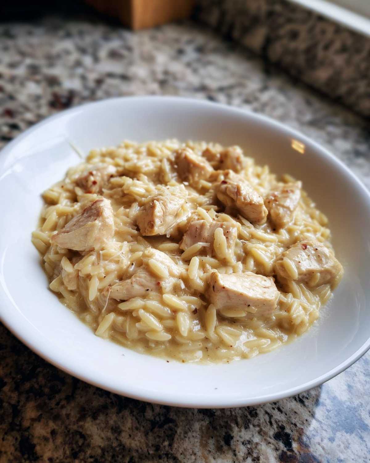 A white bowl filled with creamy Instant Pot Creamy Chicken and Orzo, featuring tender chicken chunks.