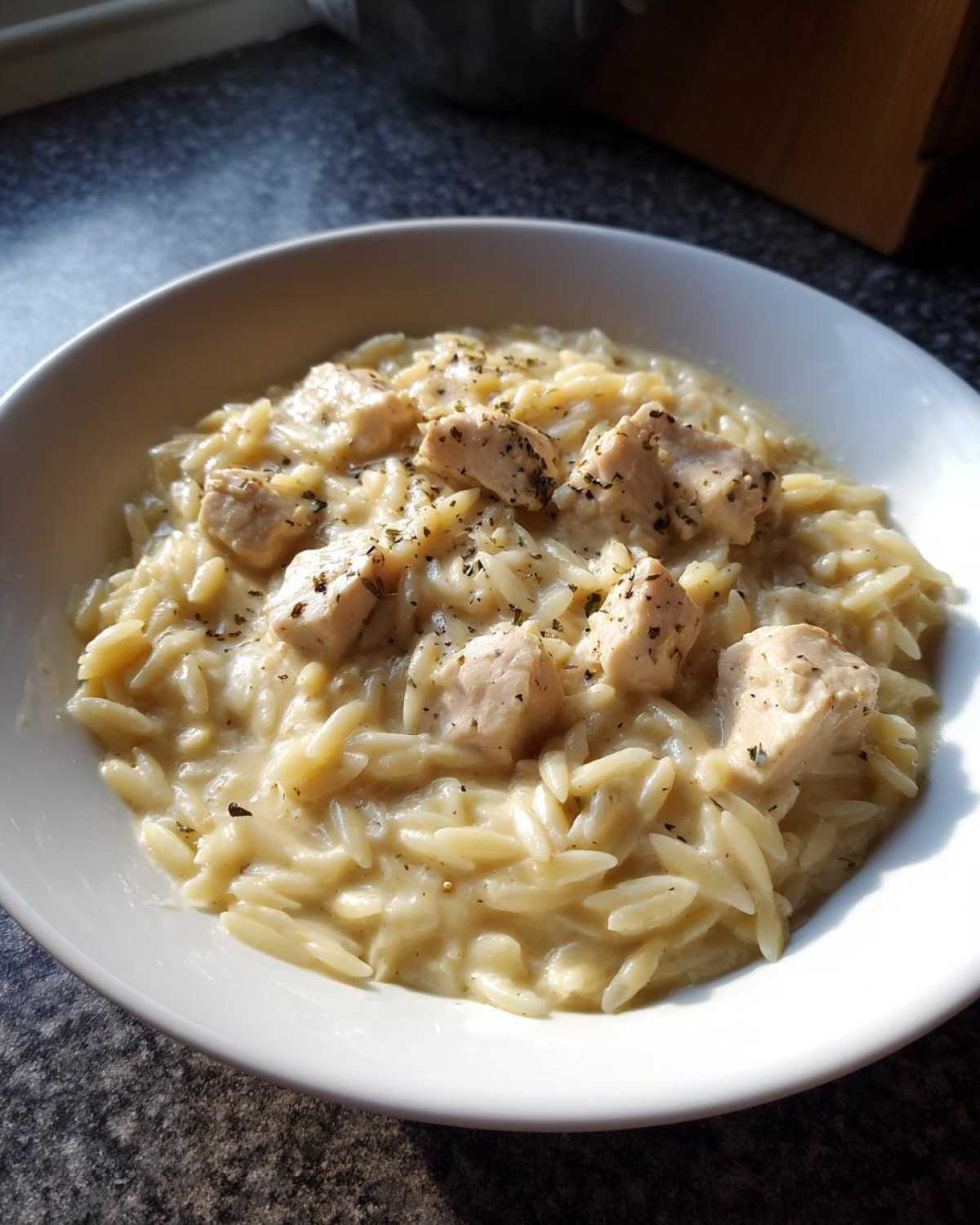 Close-up of Instant Pot Creamy Chicken and Orzo served in a white bowl, topped with herbs.