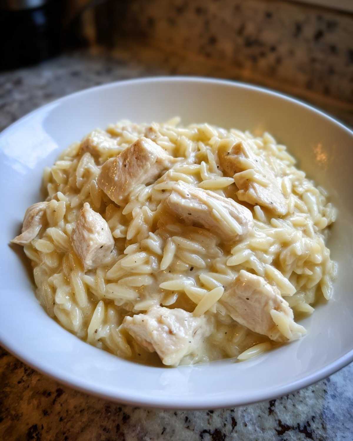 Close-up of a white bowl filled with creamy Instant Pot Creamy Chicken and Orzo, featuring chunks of cooked chicken.