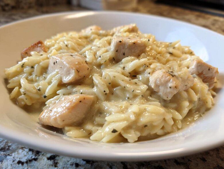 Close-up of a serving of Instant Pot Creamy Chicken and Orzo in a white bowl, featuring tender chicken pieces mixed with orzo pasta in a rich sauce.