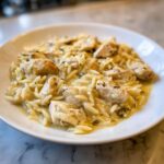 Close-up of Instant Pot Creamy Chicken and Orzo served in a white bowl on a marble surface.
