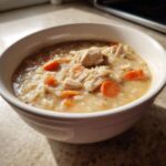 A white bowl filled with creamy Instant Pot Creamy Chicken and Rice Soup, showing shredded chicken and bright orange carrots.