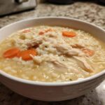 A close-up of a white bowl filled with Instant Pot Creamy Chicken and Rice Soup, showing shredded chicken, rice, and carrot slices.