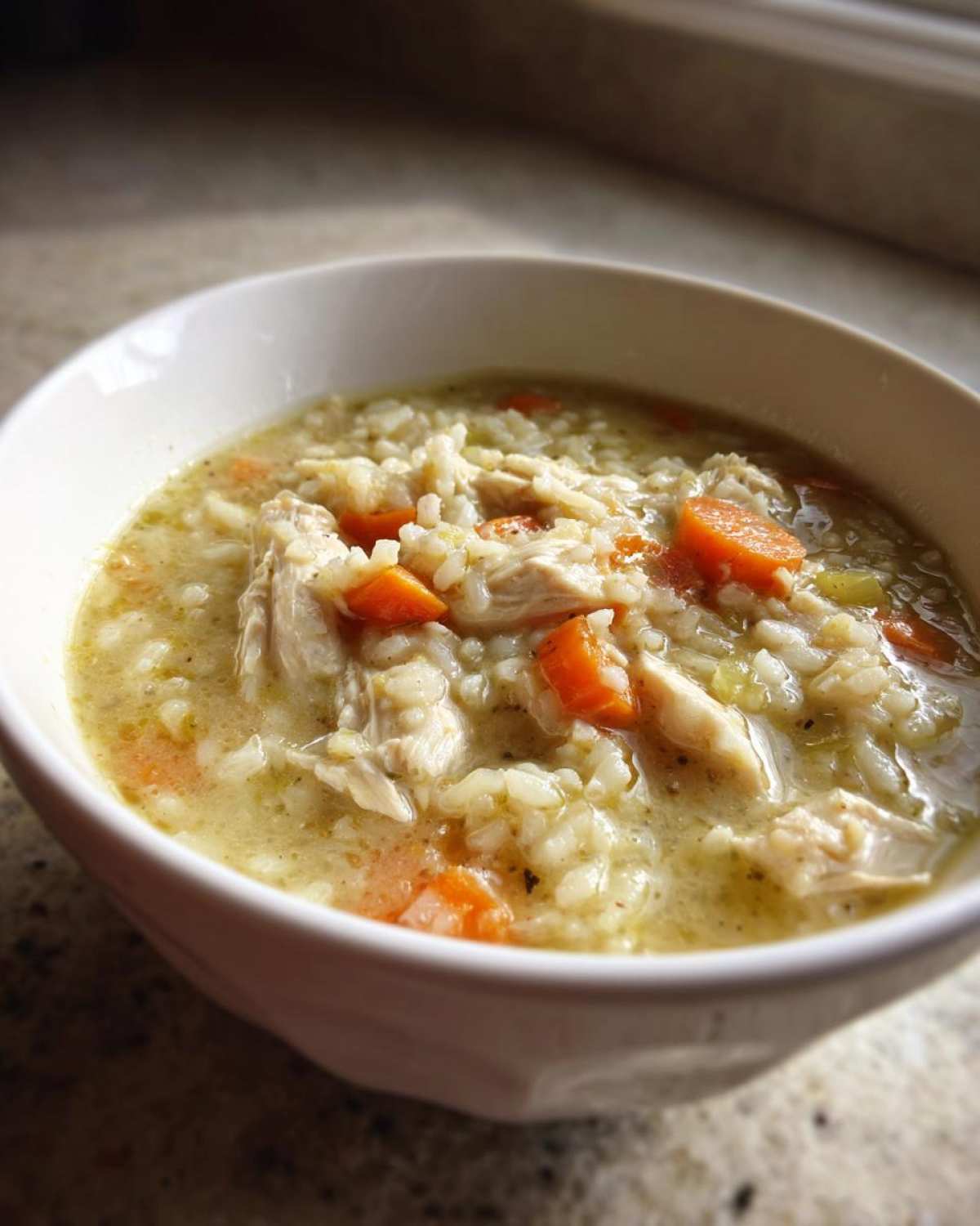 Close-up of a white bowl filled with Instant Pot Creamy Chicken and Rice Soup, showing shredded chicken, rice, and bright orange carrots.