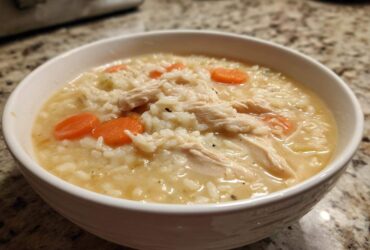 A close-up of a white bowl filled with Instant Pot Creamy Chicken and Rice Soup, showing shredded chicken, rice, and carrot slices.