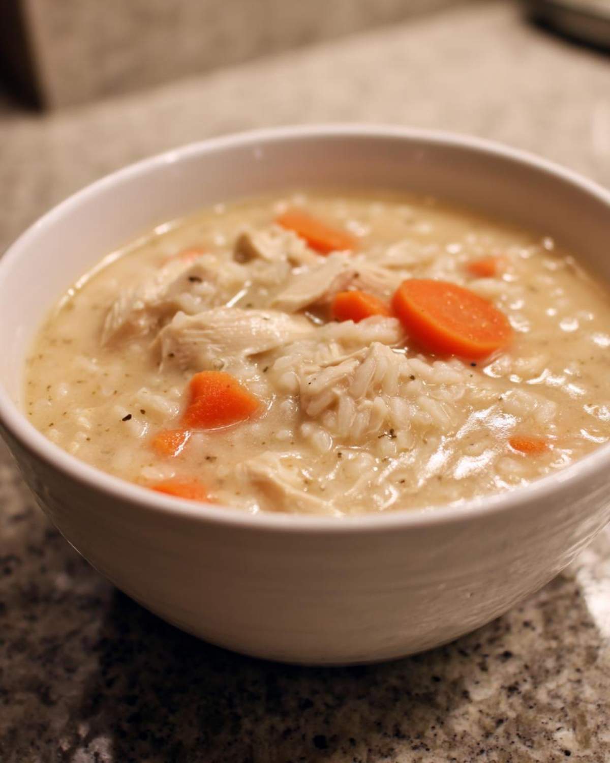 A white bowl filled with creamy Instant Pot Creamy Chicken and Rice Soup featuring shredded chicken, rice, and bright orange carrot slices.