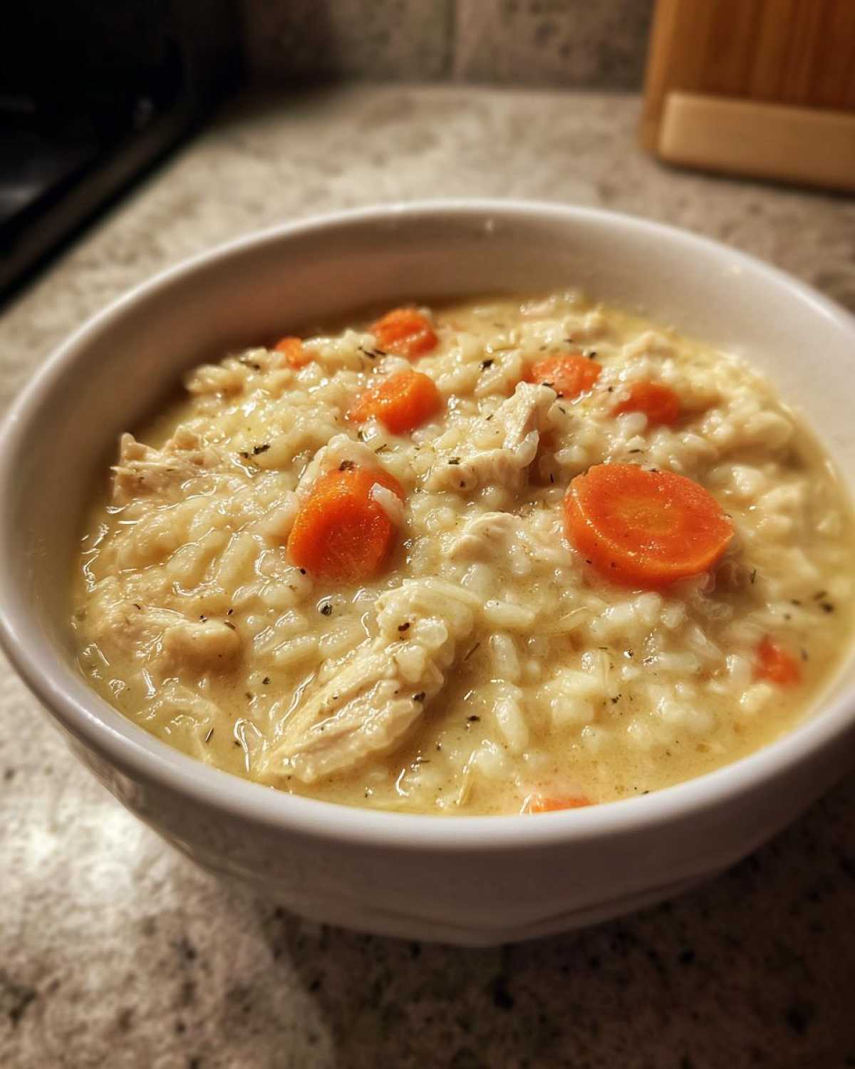 Close-up of a white bowl filled with creamy Instant Pot Creamy Chicken and Rice Soup, featuring shredded chicken, rice, and sliced carrots.