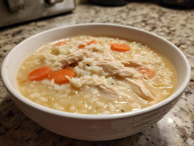 A close-up of a white bowl filled with Instant Pot Creamy Chicken and Rice Soup, showing shredded chicken, rice, and carrot slices.