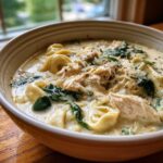 A close-up, appetizing bowl of Instant Pot Creamy Chicken Tortellini Soup topped with shredded chicken, spinach, and Parmesan cheese.
