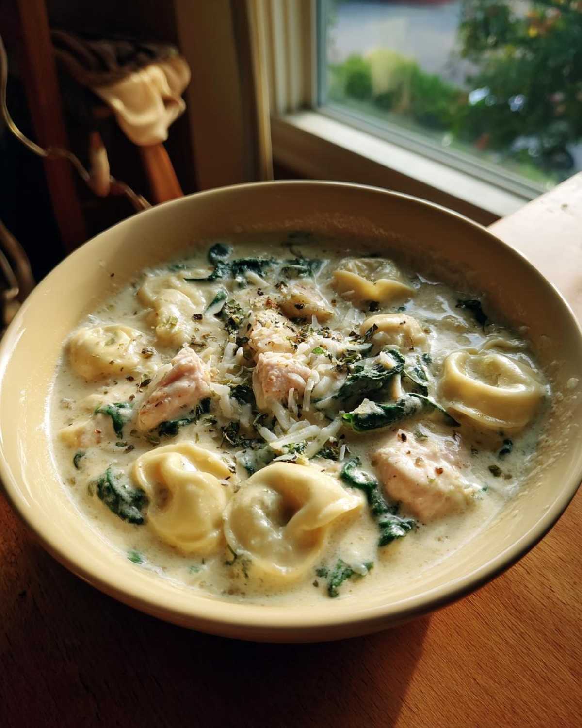 A close-up of a bowl filled with Instant Pot Creamy Chicken Tortellini Soup, featuring tortellini, chicken chunks, and spinach.
