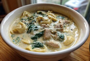 Close-up of a white bowl filled with Instant Pot Creamy Chicken Tortellini Soup, featuring tortellini, chicken chunks, spinach, and cheese.