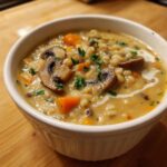 Close-up of a white bowl filled with rich Instant Pot Creamy Mushroom Barley Soup, topped with mushrooms and parsley.