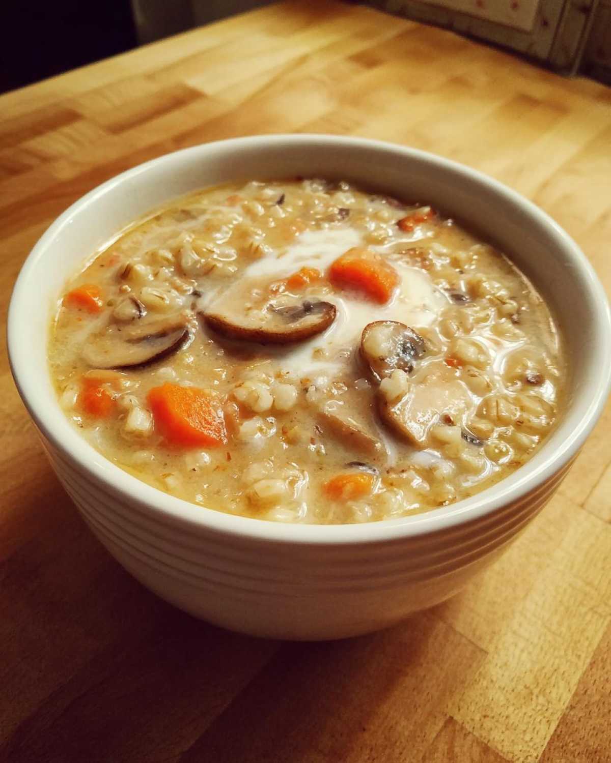 A close-up of a white bowl filled with thick Instant Pot Creamy Mushroom Barley Soup, topped with mushrooms and a swirl of cream.