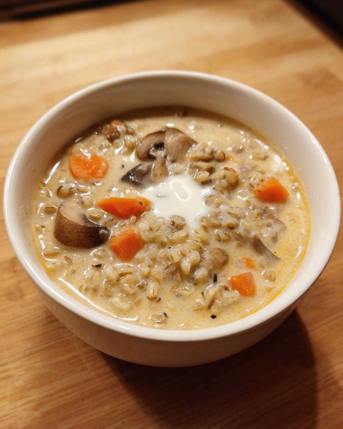 A close-up of a white bowl filled with Instant Pot Creamy Mushroom Barley Soup, topped with a dollop of cream.