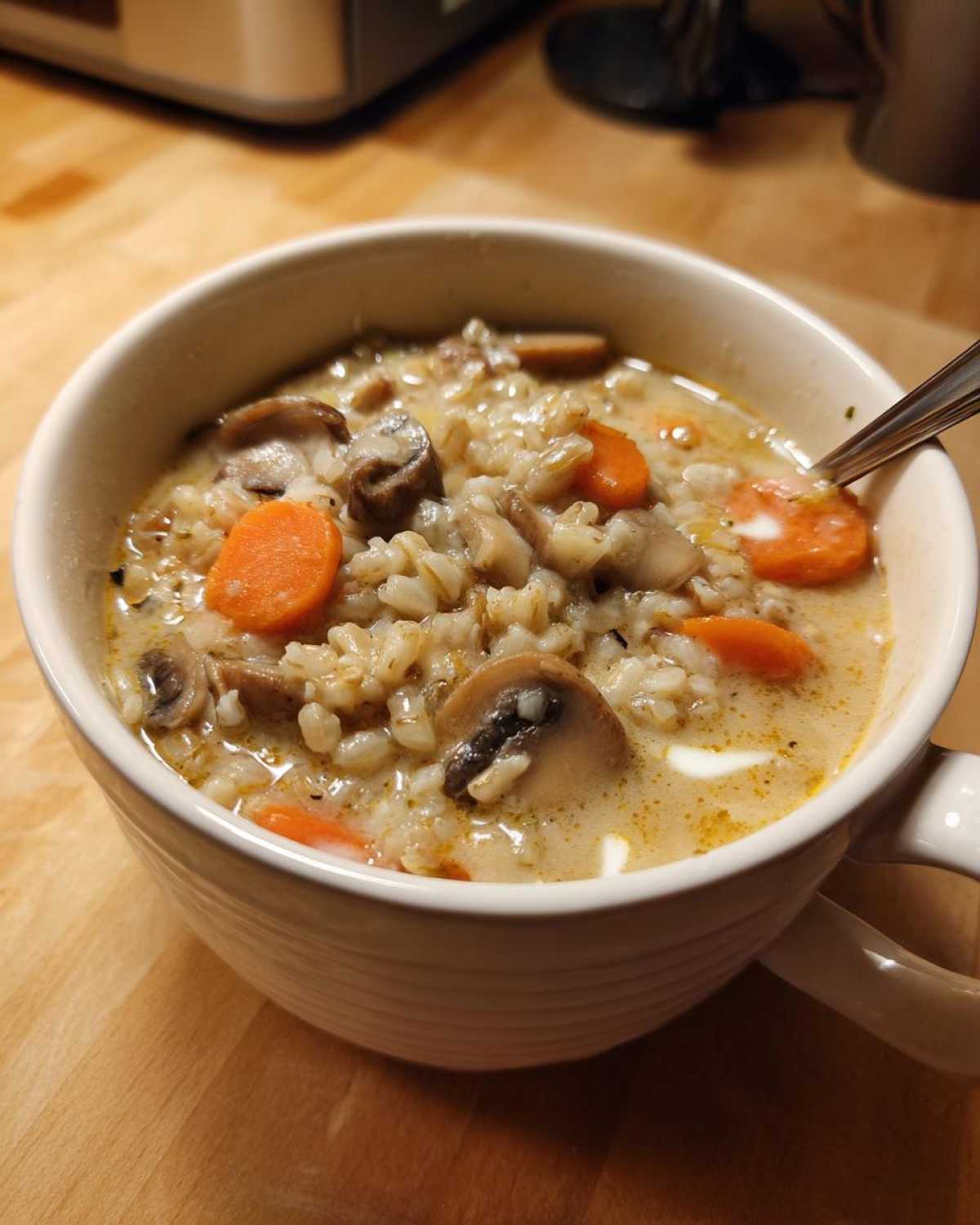 Close-up of a white mug filled with thick Instant Pot Creamy Mushroom Barley Soup, featuring barley, sliced mushrooms, and carrots.