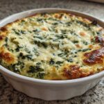 A close-up of hot Instant Pot Creamy Spinach Artichoke Dip with a golden-brown, bubbly cheese top in a white serving dish.