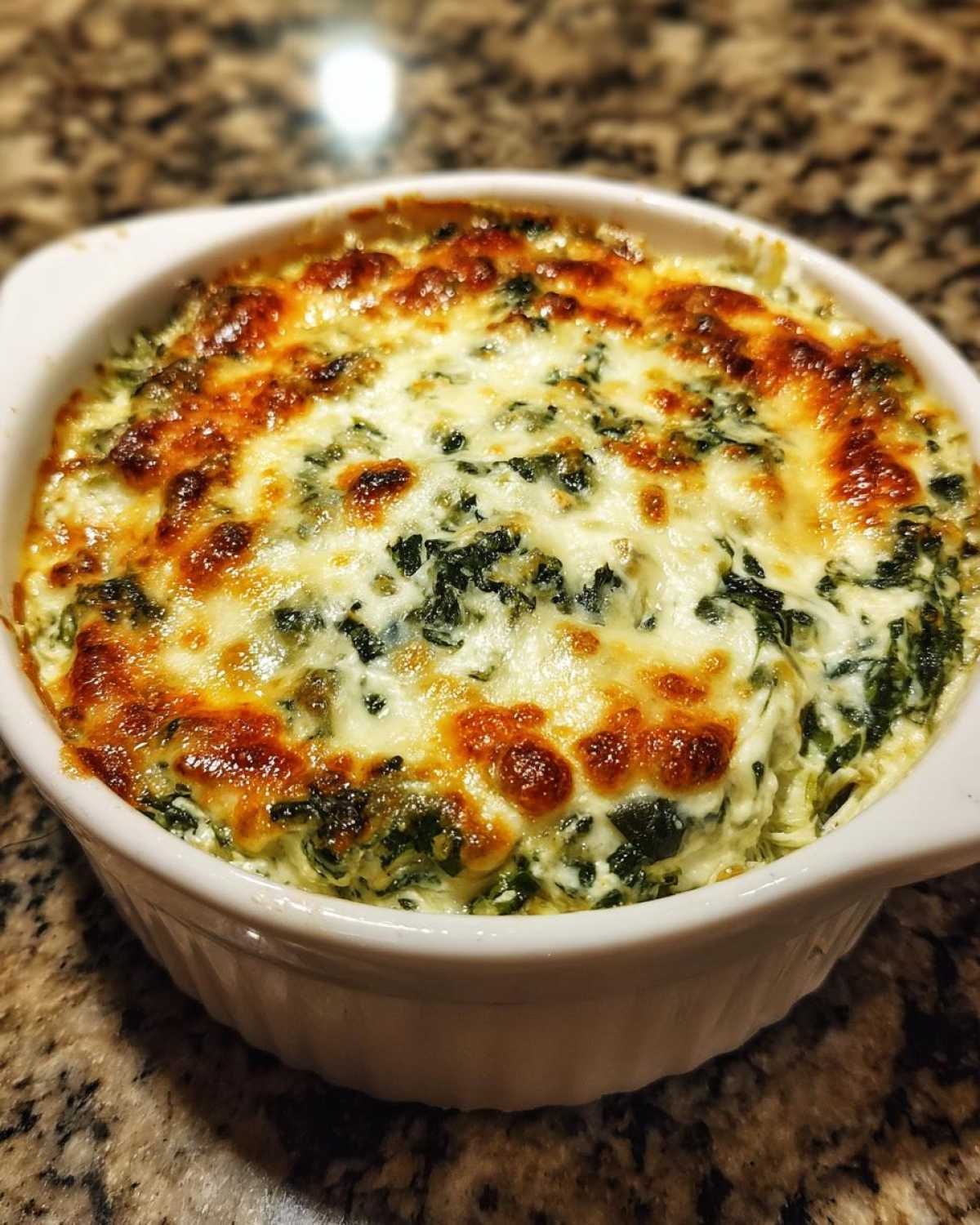 A close-up of hot Instant Pot Creamy Spinach Artichoke Dip with a bubbly, browned cheese topping in a white ramekin.