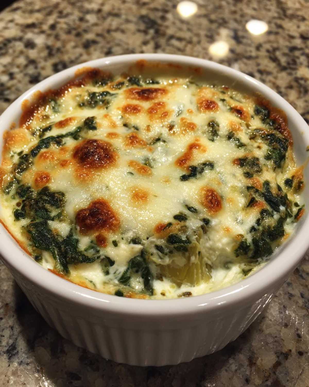 A close-up of hot Instant Pot Creamy Spinach Artichoke Dip topped with melted, bubbly, and slightly browned cheese.