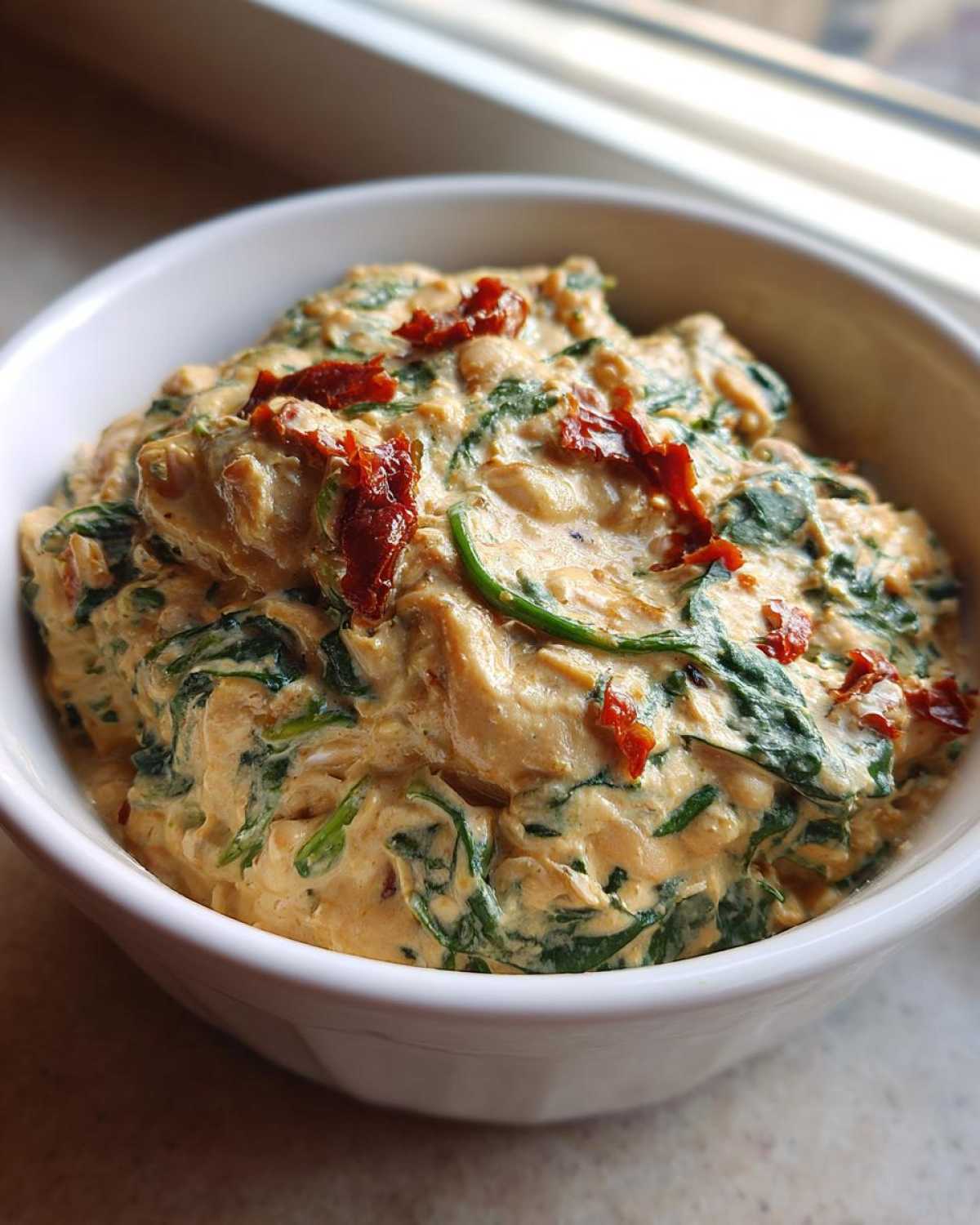 Close-up of thick Instant Pot Creamy Tuscan White Bean Soup with spinach and sun-dried tomatoes in a white bowl.