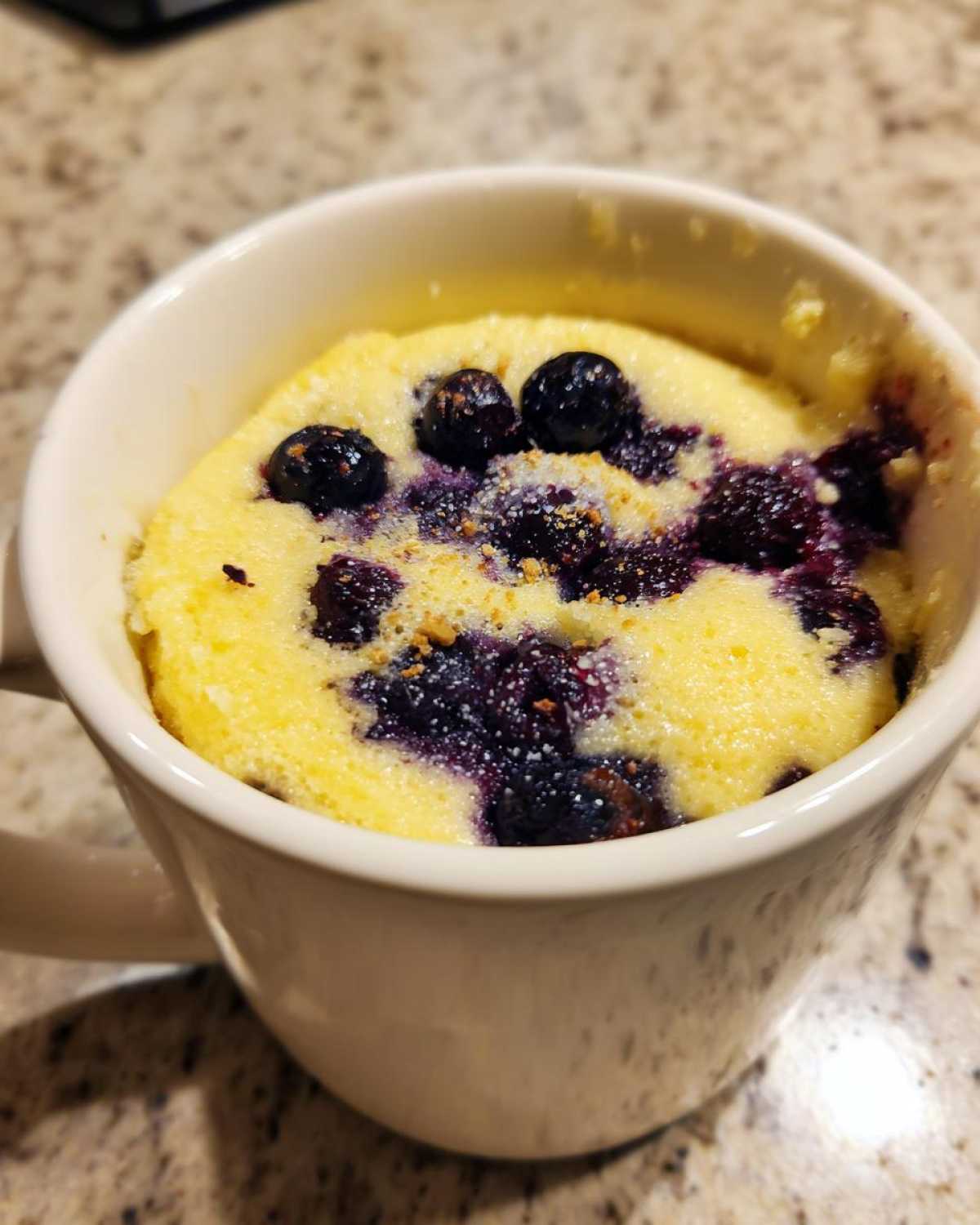 Close-up of a freshly baked Keto Blueberry Lemon Mug Cake with visible blueberries in a white mug.