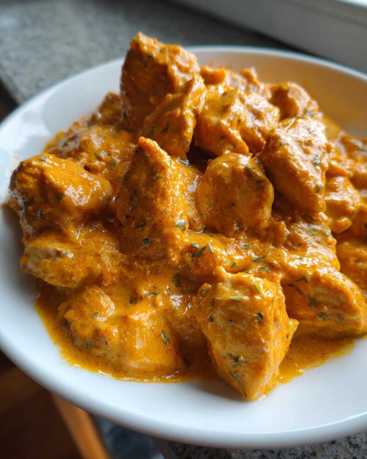 Close-up of tender chicken pieces coated in rich, orange sauce in a Keto Creamy Butter Chicken Skillet served in a white bowl.