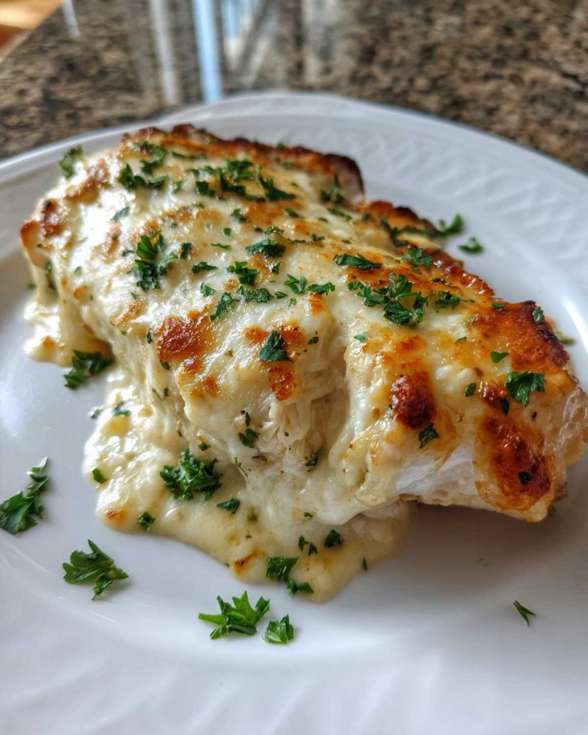 A close-up of a portion of Keto Creamy Garlic Parmesan Chicken Bake, covered in melted, browned cheese and fresh parsley.