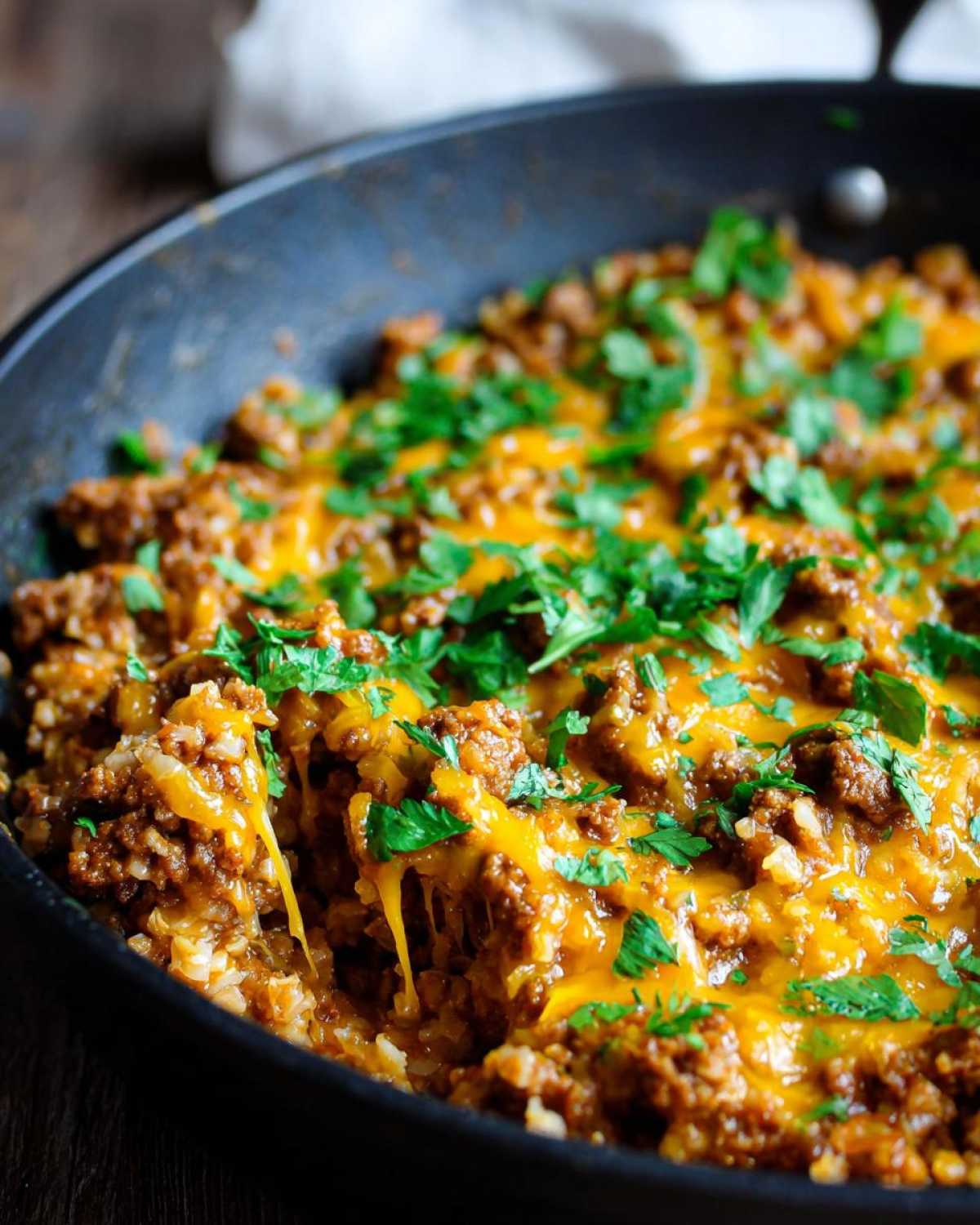 Close-up of a Keto Creamy Taco Skillet with ground meat, cauliflower rice, melted cheddar cheese, and fresh parsley.