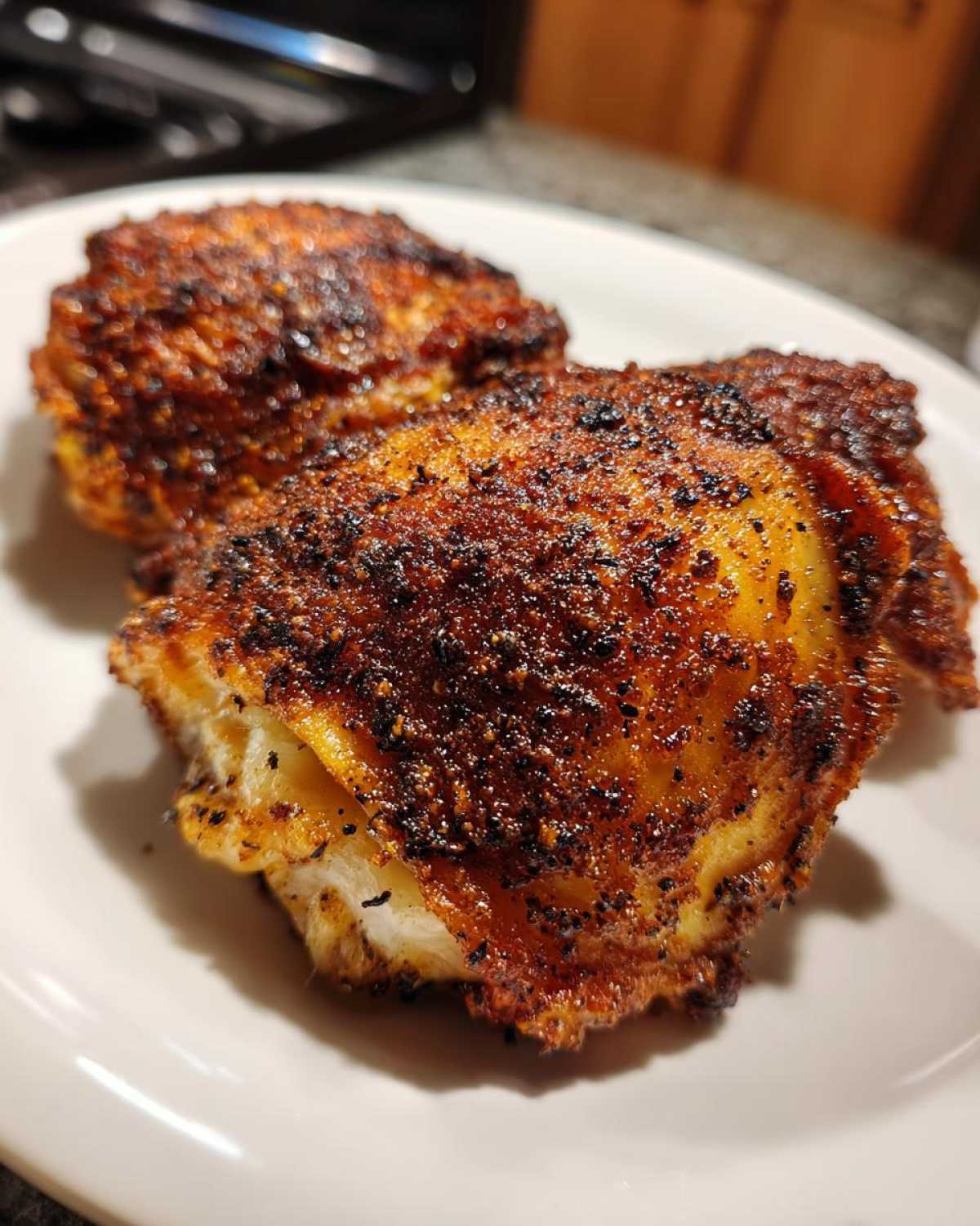 Close-up of two Keto Crispy Baked Chicken Thighs with dark, seasoned, crispy skin on a white plate.