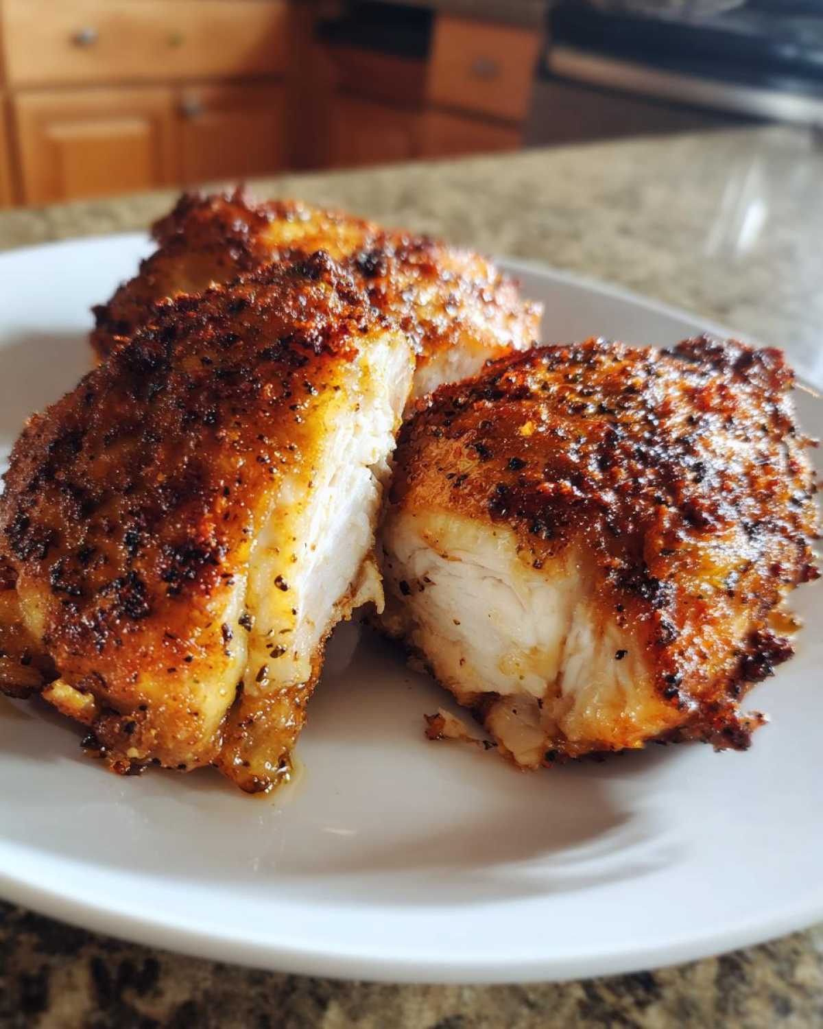 Close-up of three Keto Crispy Baked Chicken Thighs on a white plate, showing the crispy seasoned exterior and juicy white meat interior.
