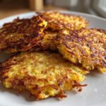Four golden brown, crispy Keto Crispy Cauliflower Hash Browns stacked on a white plate.