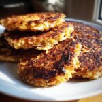 A stack of perfectly golden and crispy Keto Crispy Cauliflower Hash Browns on a white plate.