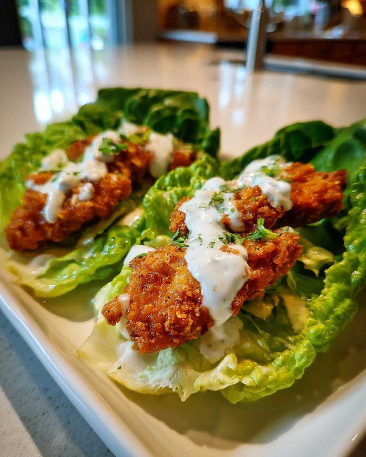 Two servings of Keto Crispy Chicken Caesar Salad Wraps featuring crispy chicken pieces on lettuce cups drizzled with white Caesar dressing.
