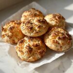A pile of freshly baked Keto Everything Bagel Cloud Bread buns topped with dark seeds, resting on parchment paper.