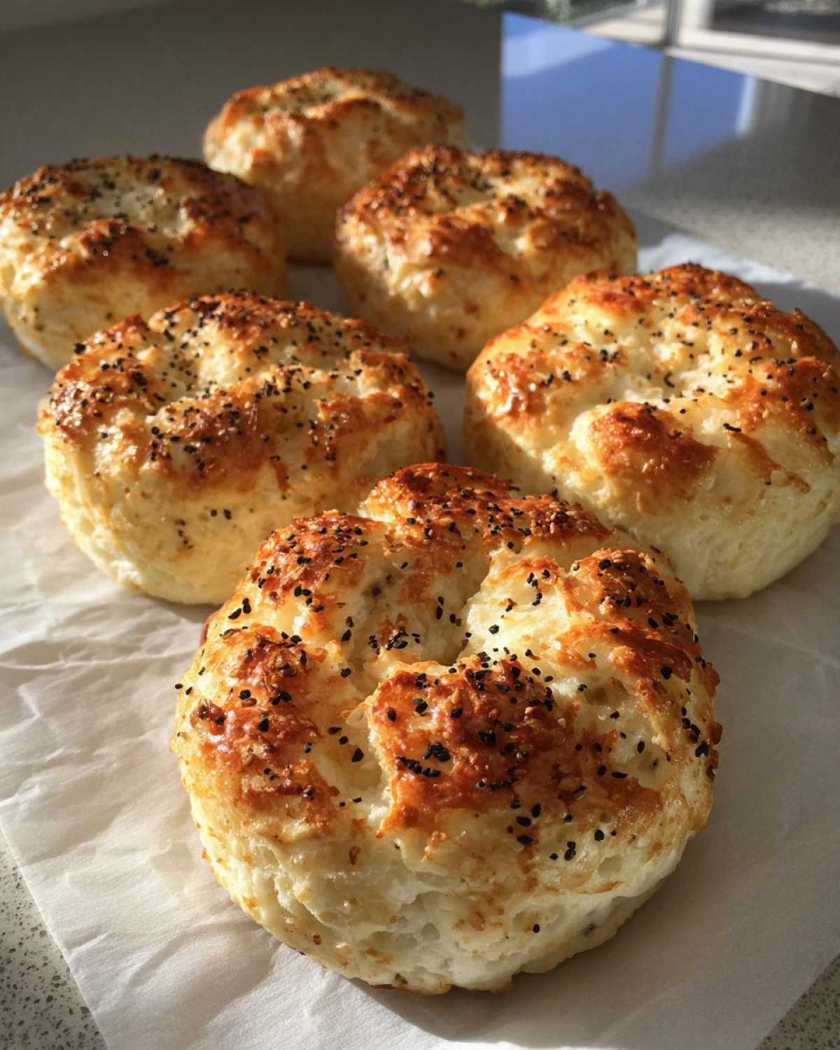 Several golden-brown Keto Everything Bagel Cloud Bread rolls topped with seeds, resting on parchment paper.