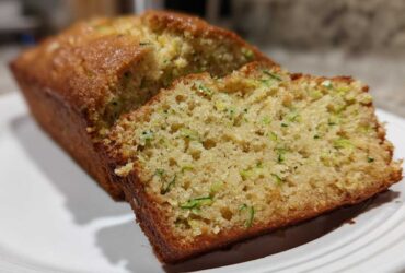 Close-up of a freshly baked Zucchini Bread loaf with one slice cut, showing moist texture and green shreds of zucchini.