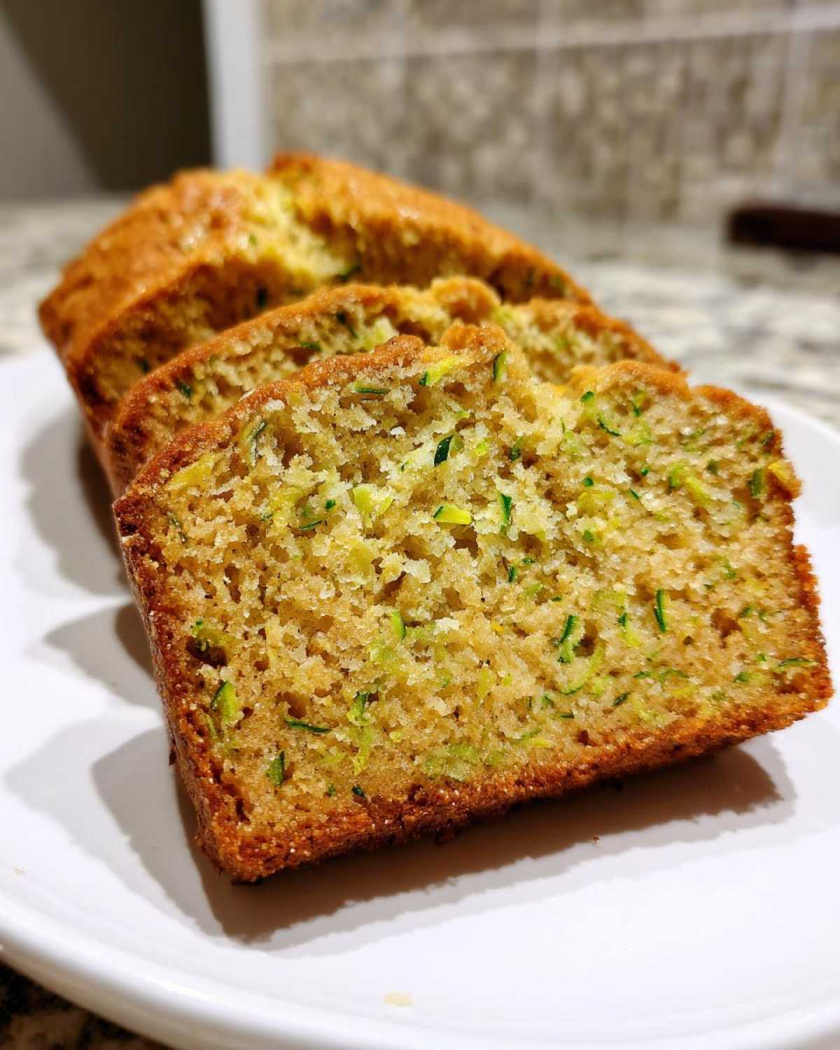Close-up of moist, sliced Zucchini Bread showing visible shreds of green zucchini throughout the crumb.