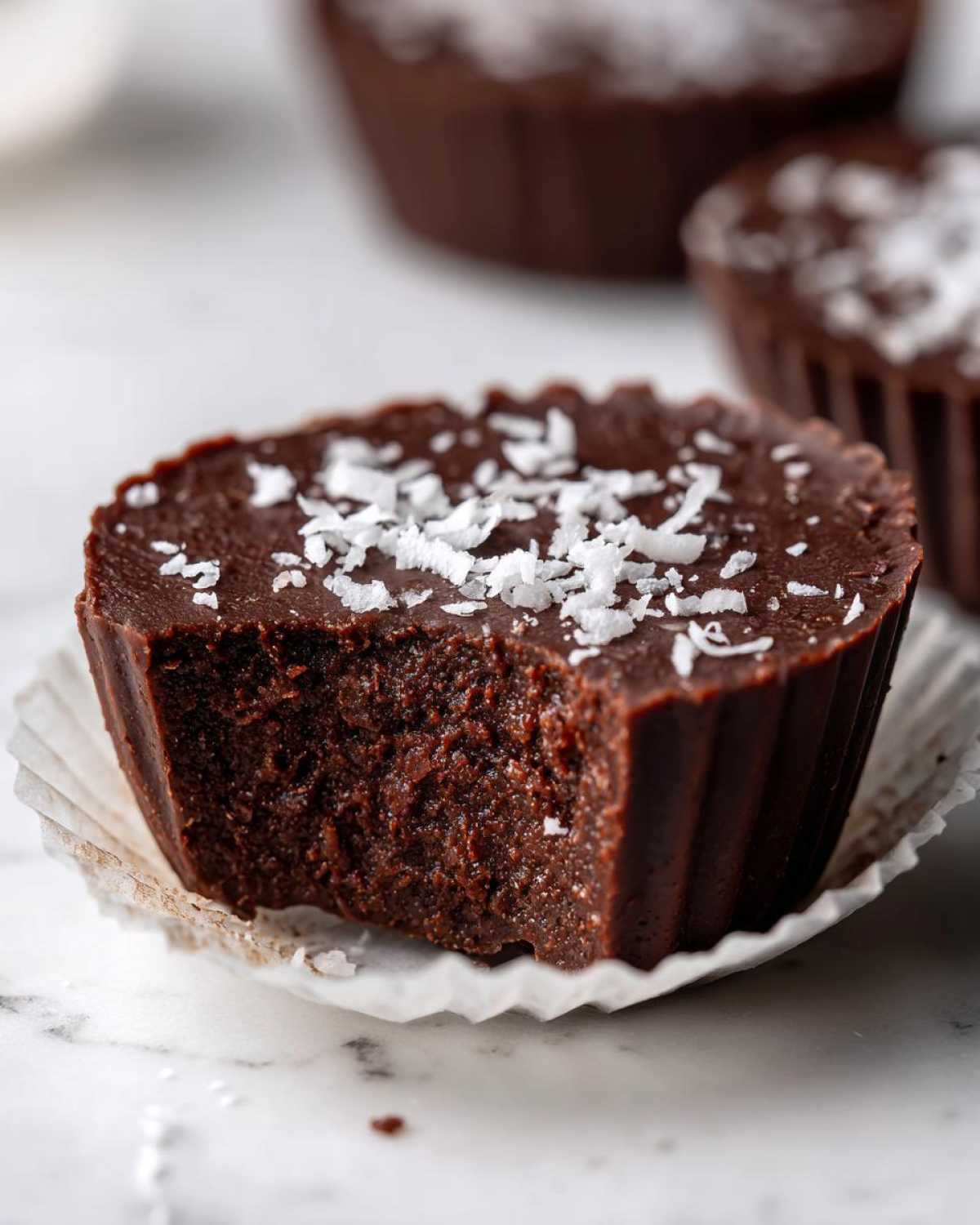 A close-up of one No-Bake Chocolate Coconut Protein Cup with a bite taken out, topped with shredded coconut.