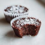A close-up of a No-Bake Chocolate Coconut Protein Cup with a bite taken out, topped with shredded coconut.