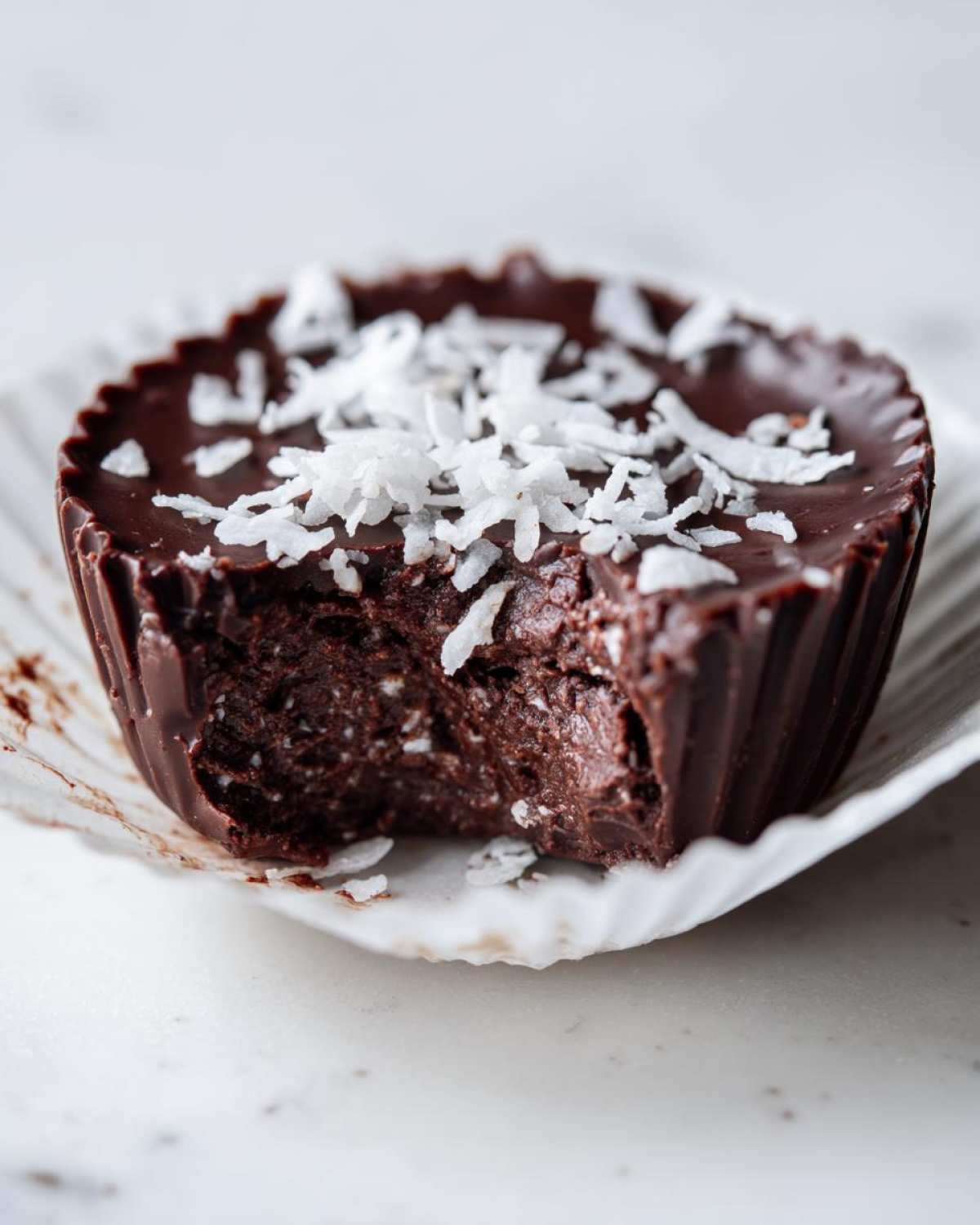 Close-up of a No-Bake Chocolate Coconut Protein Cups with a bite taken out, showing the rich filling and coconut flakes.
