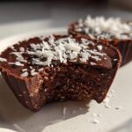 Close-up of a No-Bake Chocolate Coconut Protein Cups with a bite taken out, showing the textured interior and coconut flakes.