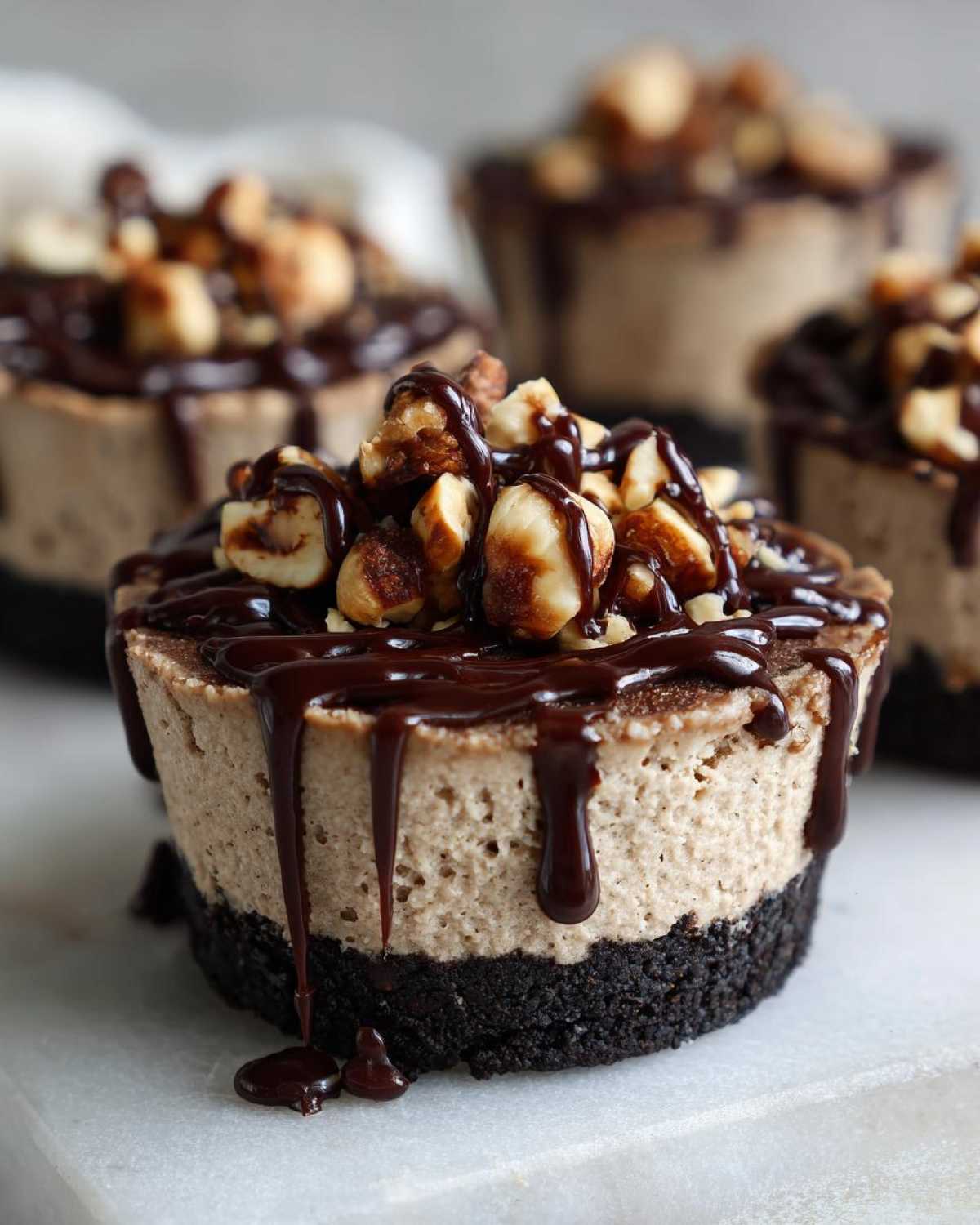 A close-up of a No-Bake Chocolate Hazelnut Cheesecake Cup with a dark crust, creamy filling, chocolate drizzle, and chopped hazelnuts on top.
