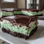 A close-up of a layered No-Bake Chocolate Mint Icebox Bars slice with chocolate crust, mint filling, and chocolate ganache.