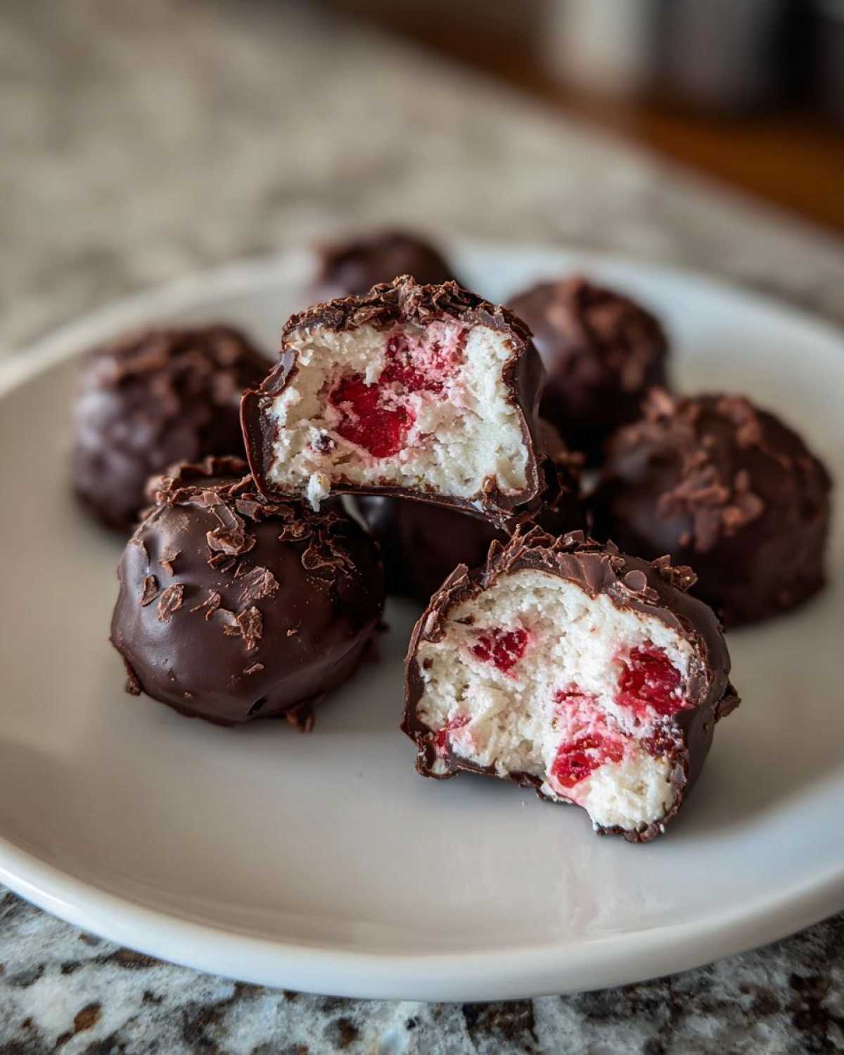 Close-up of No-Bake Chocolate Strawberry Yogurt Clusters, showing the creamy white center with red fruit pieces inside a chocolate shell.