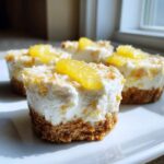 Four individual No-Bake Lemon Coconut Cheesecake Cups with a graham cracker crust and lemon slice garnish.
