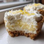 A bite taken out of a No-Bake Lemon Coconut Cheesecake Cup showing the creamy filling and graham cracker crust.